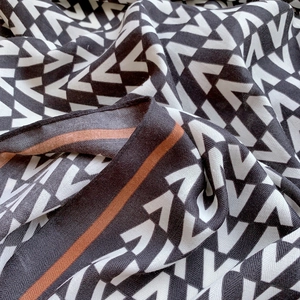 Detail of luxury silk scarf showing intricate black and white V-pattern and brown border