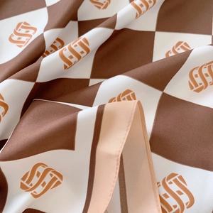 Detail shot of checkered silk scarf with warm orange accents and rolled hem finish