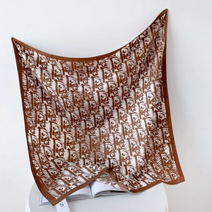 Detail of elegant brown and cream silk scarf with a full monogram print draped over a chair
