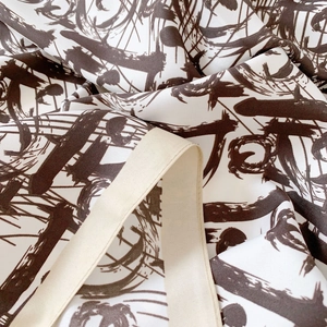 Detailed shot of white silk scarf featuring brown abstract prints and twill texture
