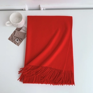 Detailed view of heavy red cashmere-feel scarf with elegant fringe trim on a white table