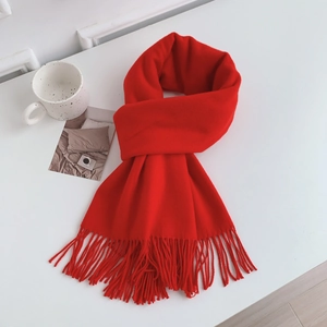 Close-up of soft thick red scarf fabric texture and long fringe tassels on white surface