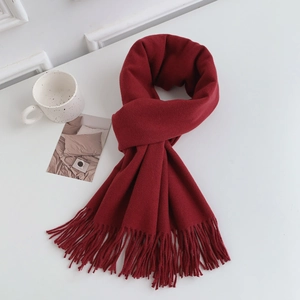 Detail shot of a thick dark red scarf with dense fringe on a cozy white desk setup