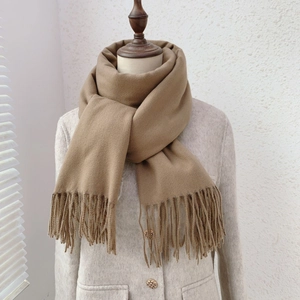 Detail shot of camel cashmere scarf with tassels styled over a beige wool coat