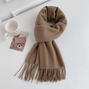 Detailed close-up of a camel cashmere-feel scarf with elegant fringe on white desk