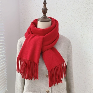 Detail of red tassel scarf on grey coat showing soft cashmere-like fabric texture