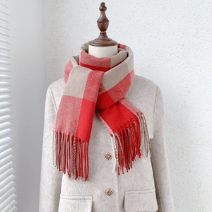 Close-up of red and beige checkered scarf with long tassels on a beige wool coat