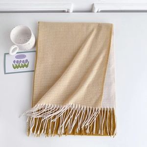Detail showing soft yellow and beige woven texture with fringe tassels on the scarf