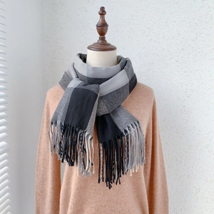 Detail of soft plaid scarf with long fringe on a wooden mannequin against white wall