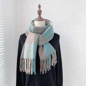 Detail of teal and grey plaid scarf with long fringe hanging from a mannequin