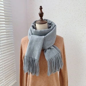 Detail shot of light grey scarf with tassel edges on display over orange knitwear