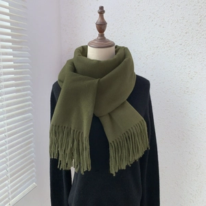 Detail of olive green cashmere-feel scarf with tassels on mannequin in a cozy setting