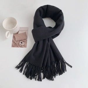 Detailed view of dark grey cashmere-feel scarf with dense fringe tassels on a white surface