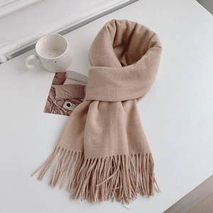 Close-up of beige pashmina scarf with long tassels and soft knit texture on white surface