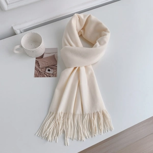 Detail view of cream cashmere-like winter scarf showing thick texture and tassel fringe