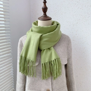 Detail of avocado green cashmere-like scarf with fringe tassels on a coat display