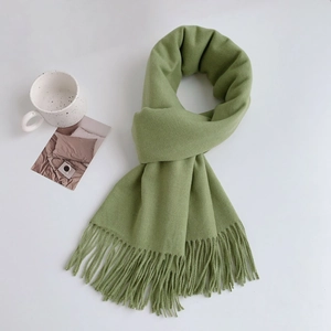 Detailed view of the soft avocado green scarf with fringed edges in a cozy setup