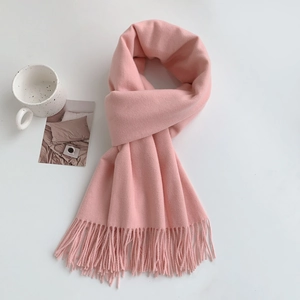 Close-up of soft pink pashmina scarf with fine tassel fringe on a warm white background