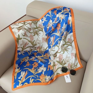 Close-up of silk square scarf with iris print and orange border on leather sofa
