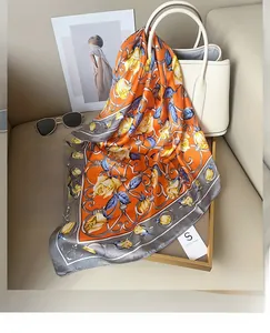 Élégant foulard en soie orange avec roses jaunes et motif chaîne noué sur un sac