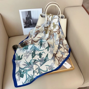 Detailed iris floral silk scarf with royal blue edges draped over a beige handbag