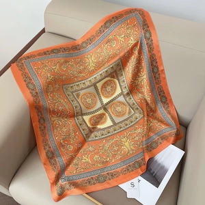 Détail d'un foulard en soie orange avec motif baroque doré et bordure de style grec