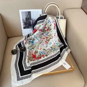 Détail d'un carré de soie imprimé floral avec bordure géométrique drapé sur un sac blanc