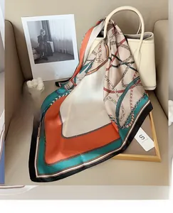 Detail of silk-feel scarf with chain and tassel patterns draped over a white handbag