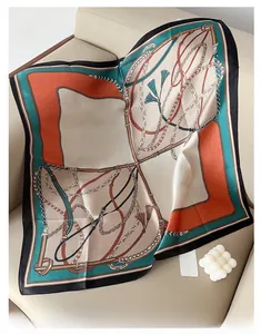 Close-up of elegant satin square scarf with tassel and chain prints on a leather sofa