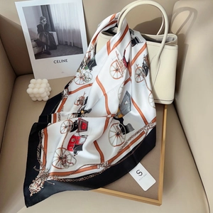 Classic silk scarf with carriage pattern draped on a cream leather handbag