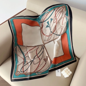 Detail of silk satin scarf with equestrian chain patterns and tassels on a sofa