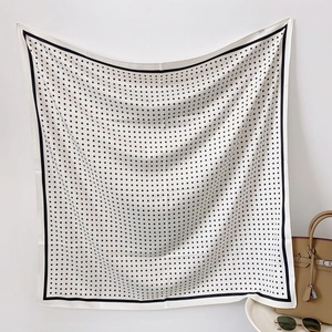 Elegante foulard in seta a pois bianchi con bordo nero posto su una borsa beige