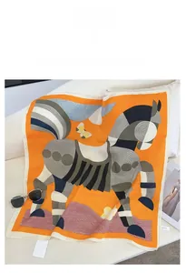 Detail of silk-feel scarf with orange horse and butterfly print on a white sofa