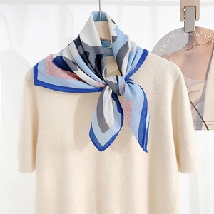 Detail of blue and white geometric printed silk scarf tied on a cream knit sweater