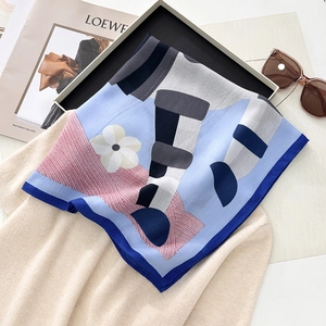 Detail of square silk scarf with blue floral prints draped over beige knitwear