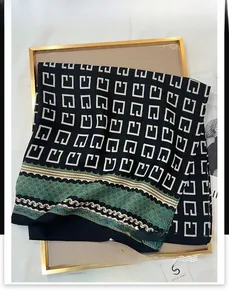 Close-up of black silk scarf with white geometric patterns and teal wavy border
