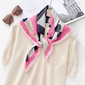 Detail of printed silk scarf tied on a beige sweater with polka dots and stripes