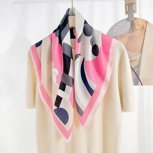 Close-up of a printed silk scarf with pink and black geometric patterns on a beige knit top