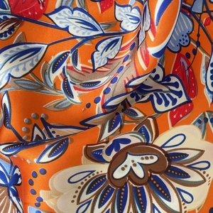 Detailed macro shot of silky floral fabric with vibrant orange and navy botanical patterns