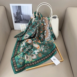 Nahaufnahme eines dunkelgrünen Paisley-Seidenschals an einer weißen Handtasche im Detail