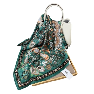Luxuriöser grüner Seidenschal mit Paisley-Blumenmustern drapiert auf einer Tasche