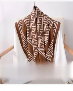 Close-up of caramel silk scarf with white Greek Key pattern draped over a white shirt