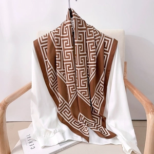 Detail of a geometric Greek key pattern silk scarf styled over a white chiffon shirt