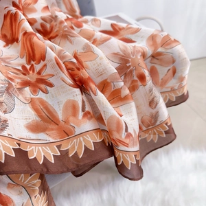 Detail of orange floral silk satin scarf featuring elegant print and brown lace trim edge