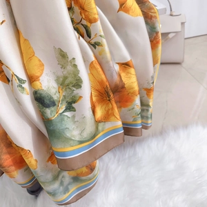 Dettaglio di sciarpa in seta con fiori arancioni e bordi a righe su borsa beige