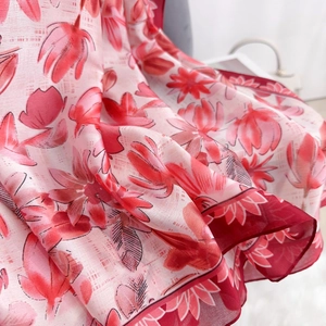 Detailed close-up of floral print silk scarf with smooth texture and red hemmed edges