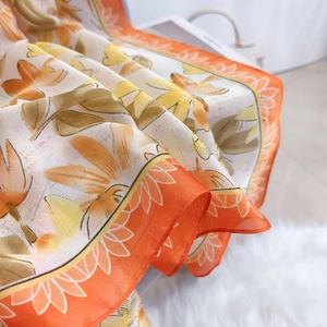 Close-up of floral print silk scarf featuring sunflower patterns and orange borders