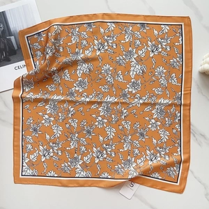 Orange faux silk square scarf with floral print and black border on marble surface