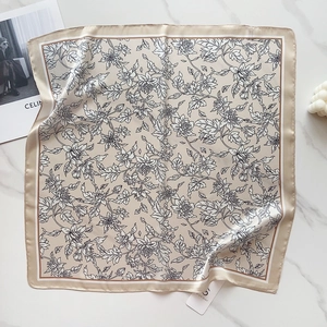 Flat lay of champagne satin silk scarf with black floral print on marble background