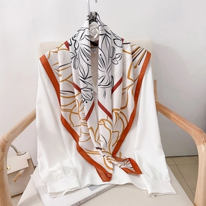 Elegant floral silk square scarf with orange borders on a minimalist white shirt and chair